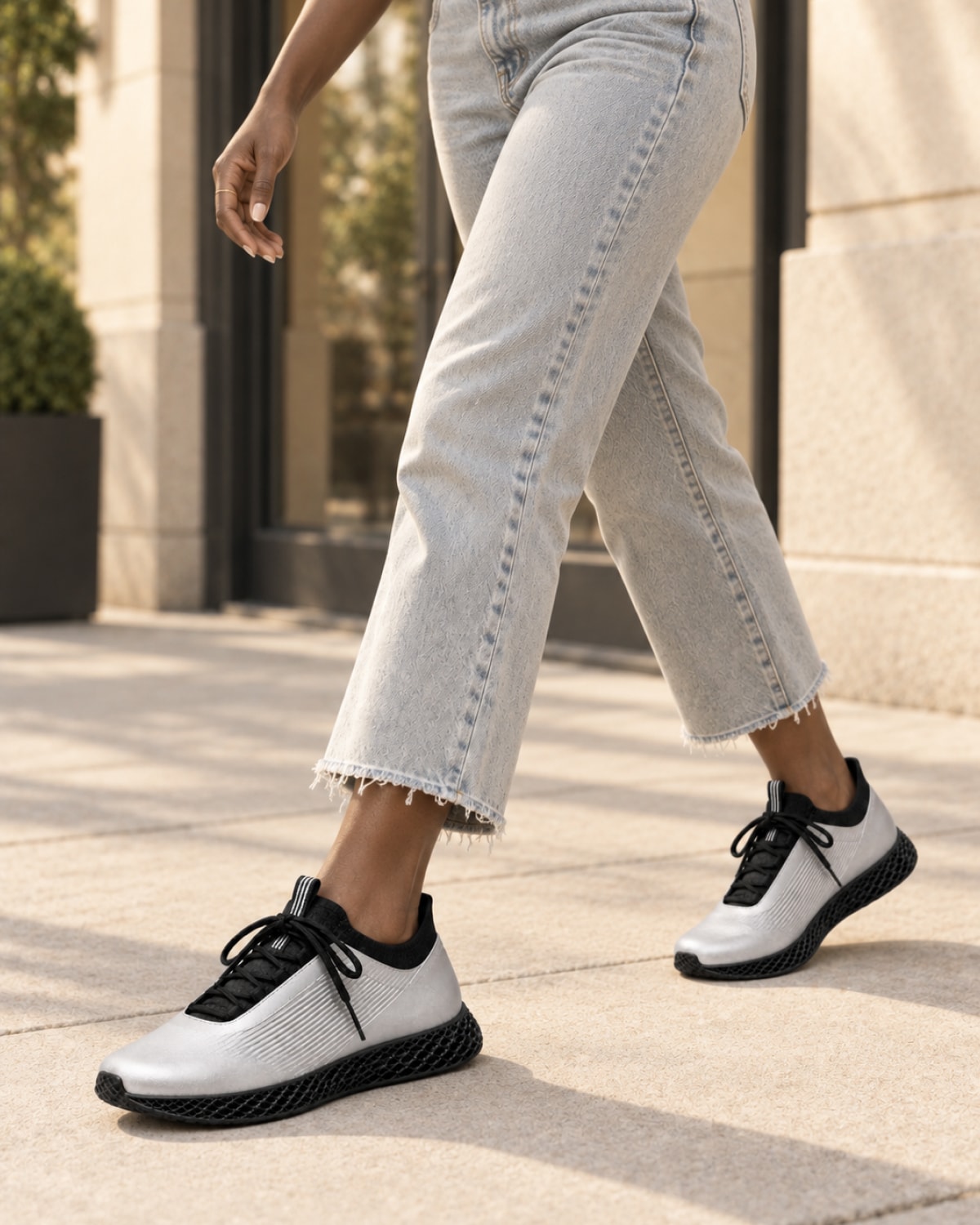 A person walking outdoors wearing light gray cropped jeans and white athletic sneakers with black details, shown from the waist down on a paved walkway.
