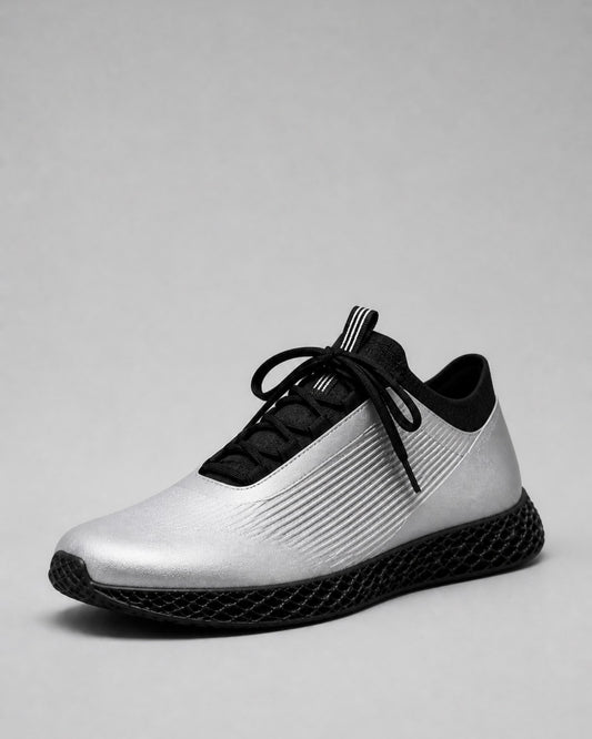 A single athletic sneaker shown from a side profile view on a neutral gray background. The shoe features a metallic silver upper with black ribbed detailing, black laces, a black collar, and a black textured sole.