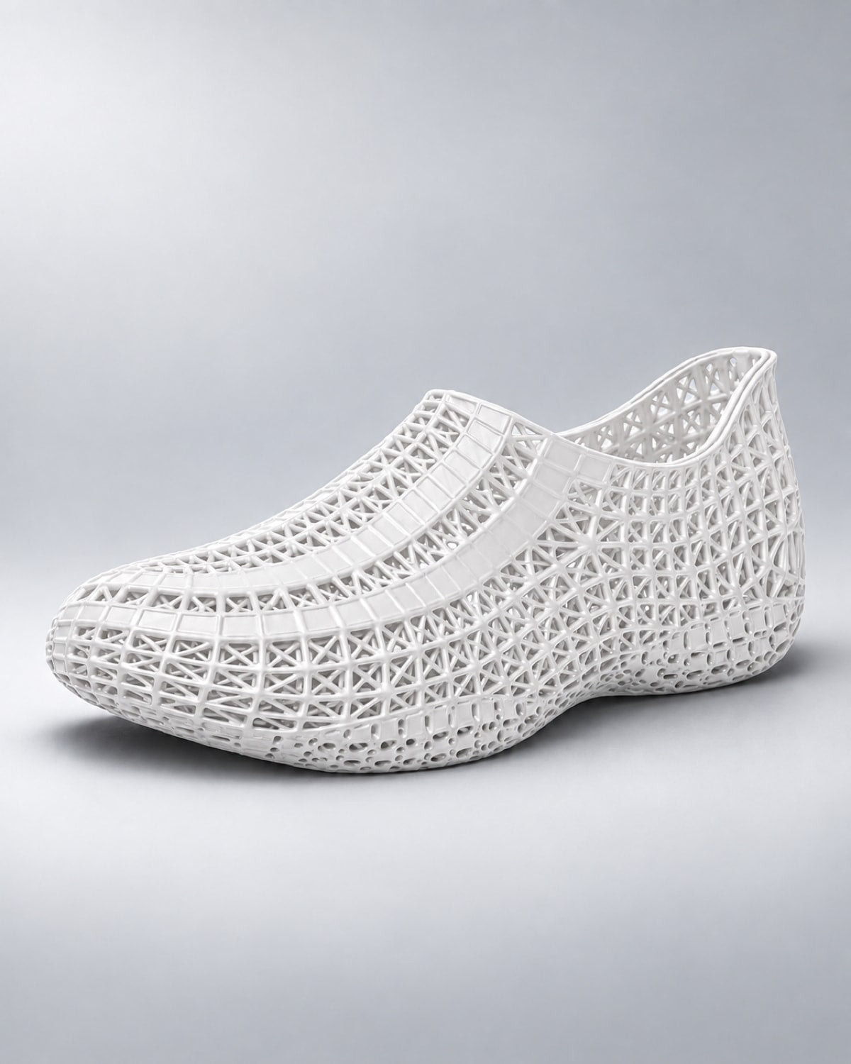 A white slip-on shoe with an intricate, open geometric lattice pattern, shown from a three-quarters angle on a light gray gradient background.