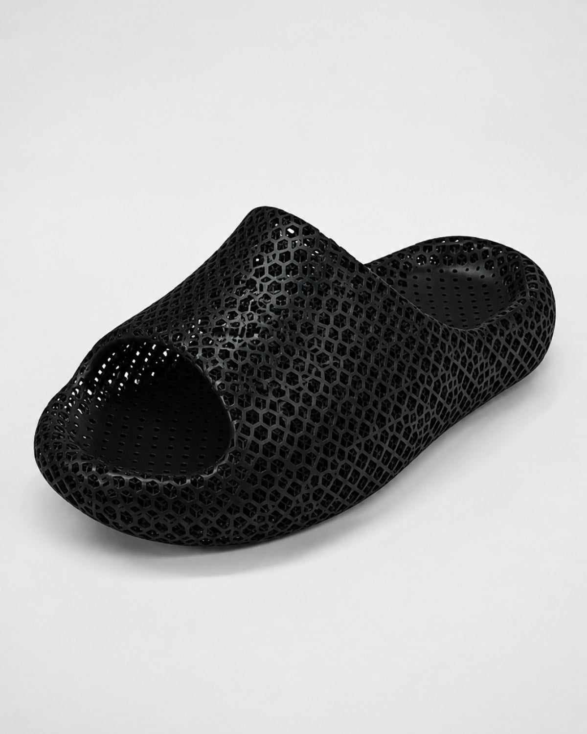 A single black open-toe slip-on clog-style shoe with a textured, perforated surface pattern, photographed on a light gray studio background.