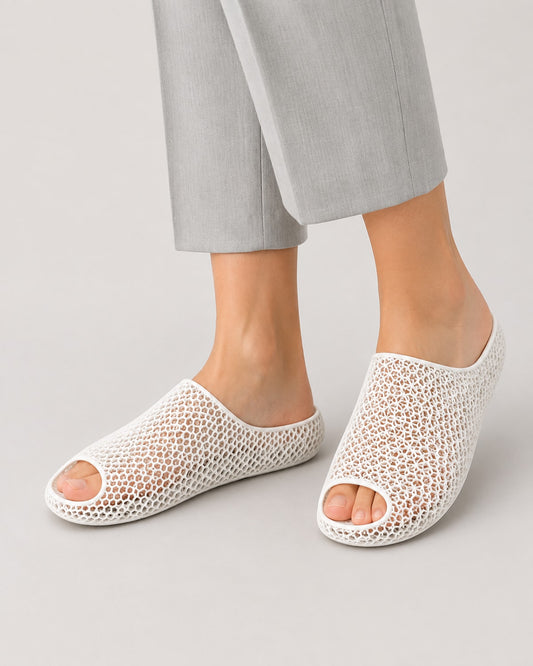 White open-toe mesh slip-on shoes worn with light gray cropped trousers, shown on a model against a light gray studio background.