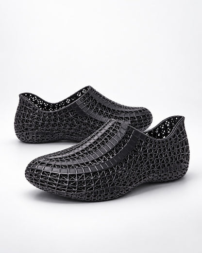 A pair of black mesh slip-on shoes with a textured, woven-like pattern, displayed on a clean white background.