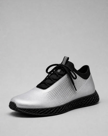 A single athletic sneaker shown from a side profile view on a neutral gray background. The shoe features a metallic silver upper with black ribbed detailing, black laces, a black collar, and a black textured sole.