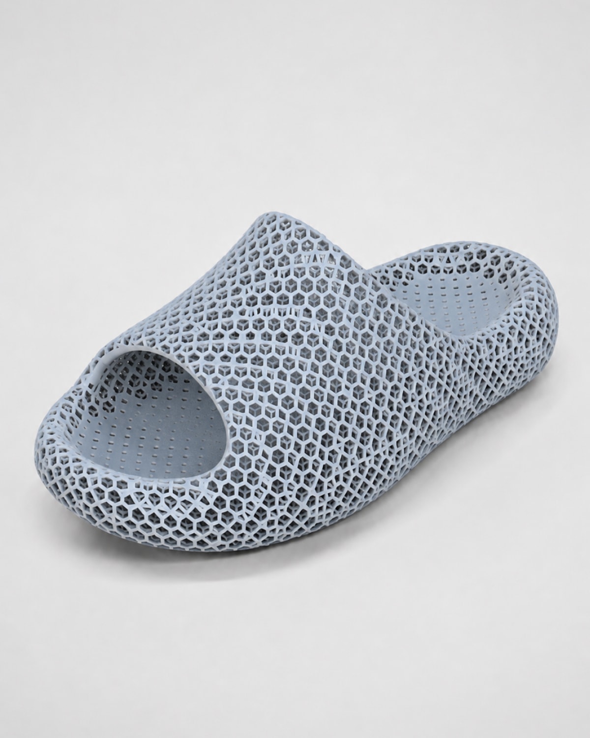 A single light blue-gray slip-on slide sandal with a distinctive 3D-printed honeycomb lattice pattern, shown on a neutral light gray background.