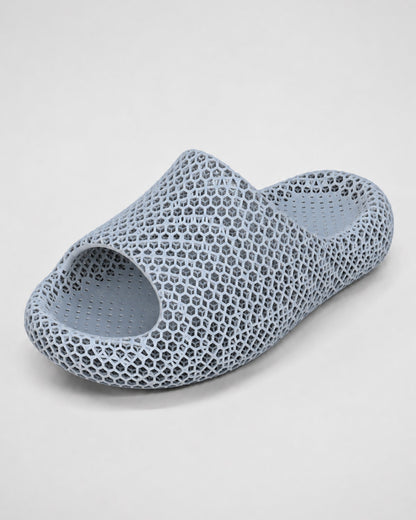 A single light blue-gray slip-on slide sandal with a distinctive 3D-printed honeycomb lattice pattern, shown on a neutral light gray background.