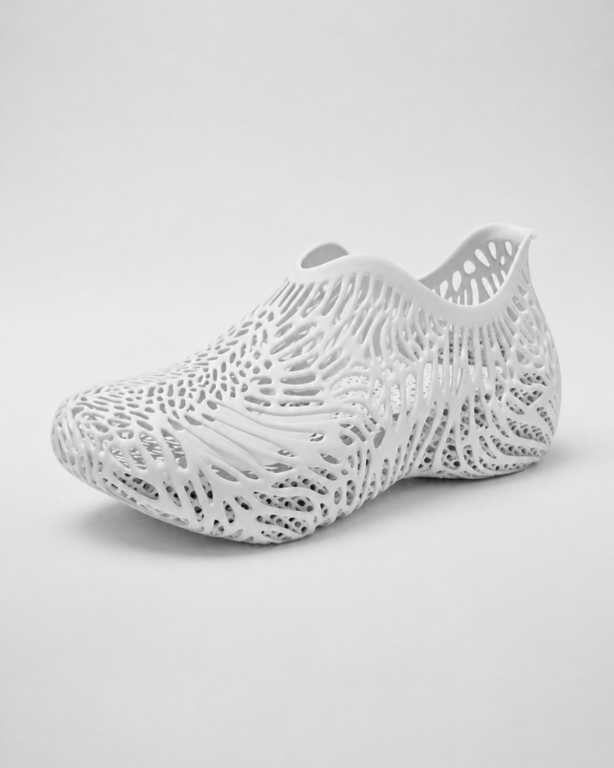 A white 3D-printed slip-on shoe with an intricate, openwork lattice pattern, shown from a side profile on a light gray background.